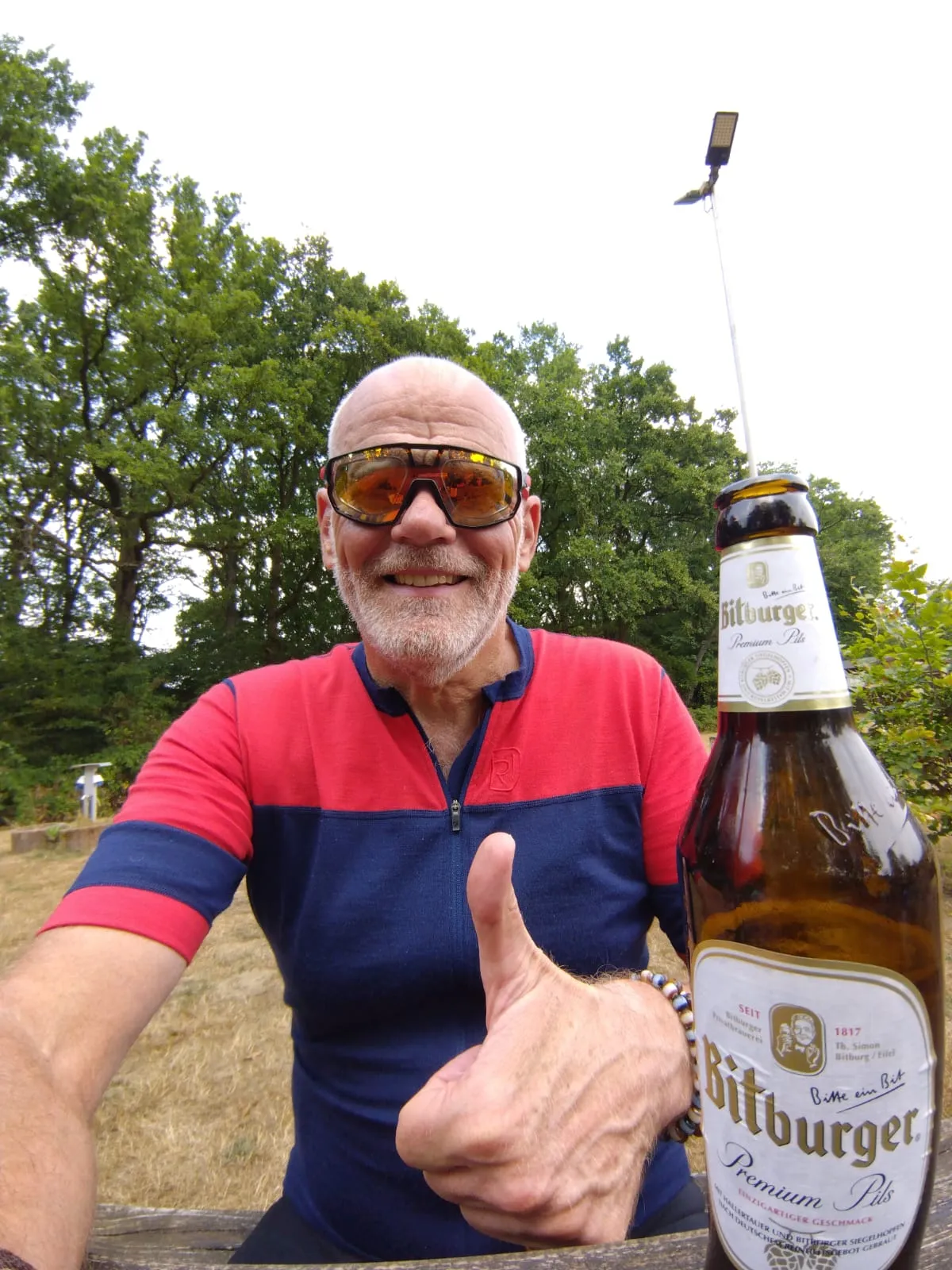 Jean-Pierre présente une bouteille de bière Bitburger au camping