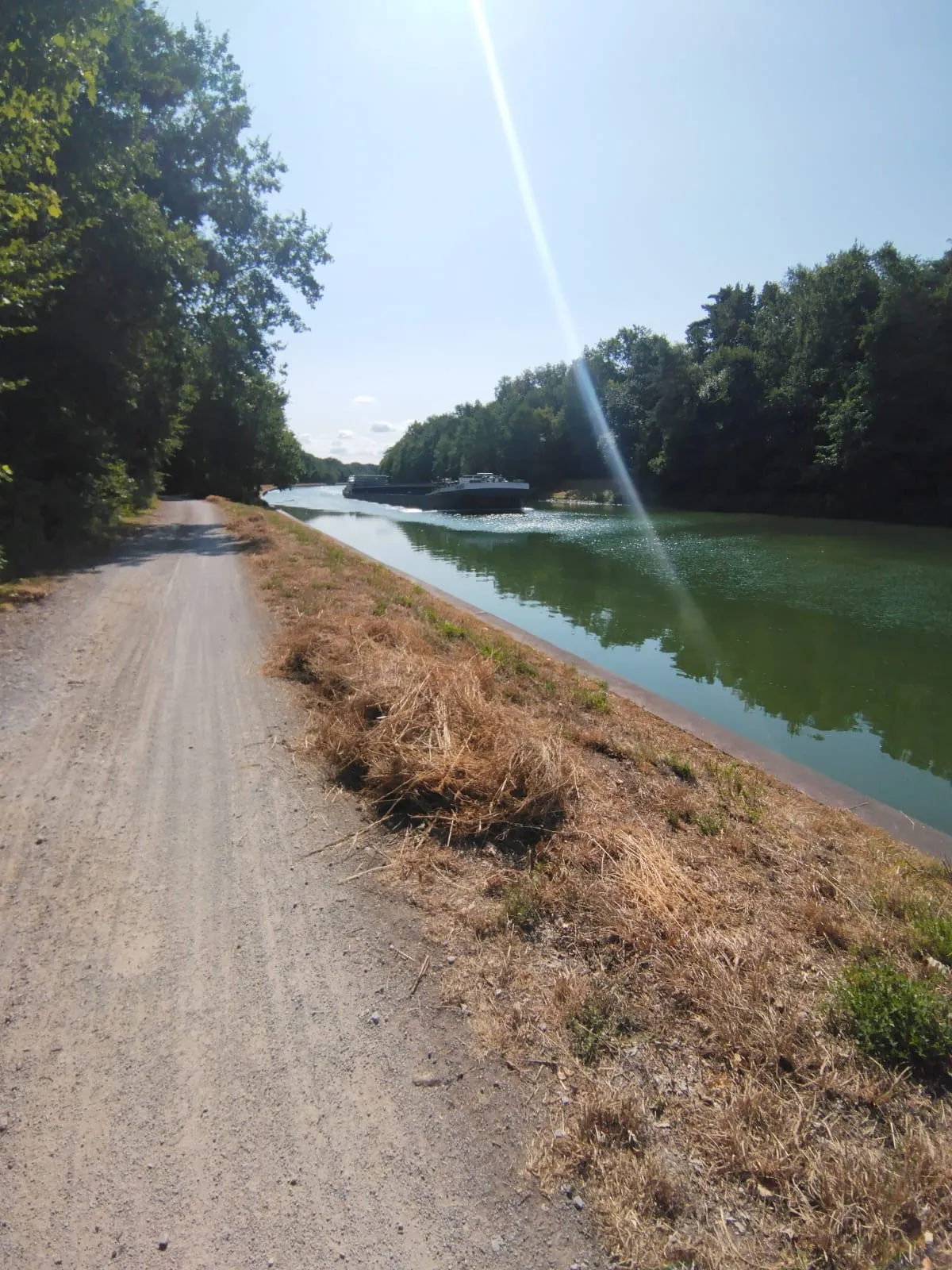 Un bateau navigue sur un canal bordé d’une piste en gravier