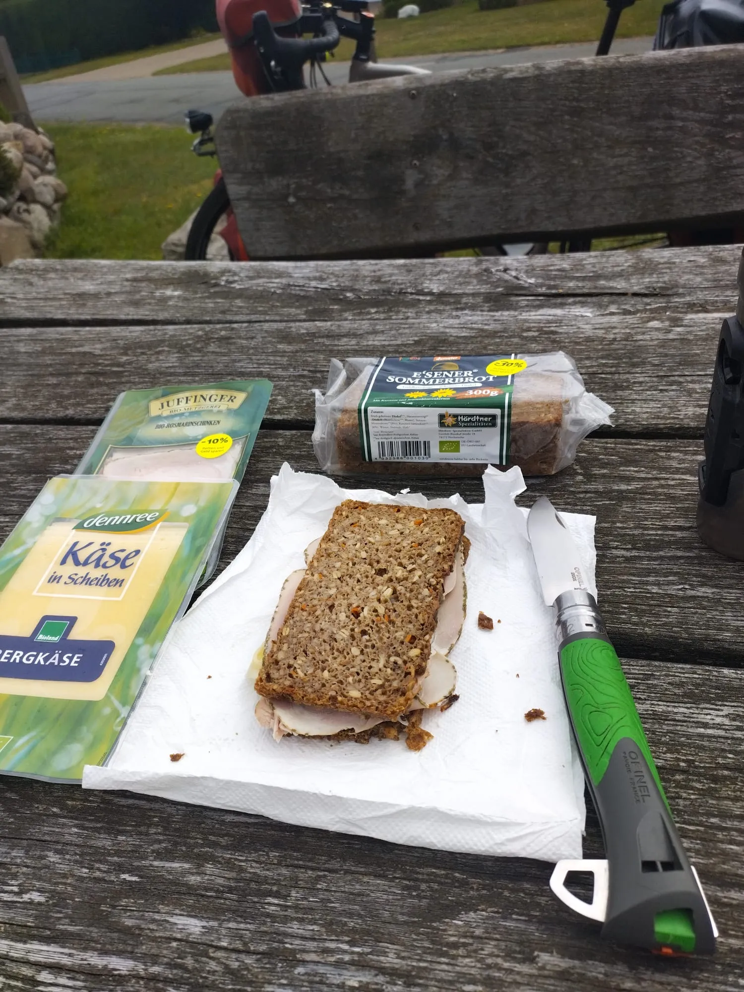 Un sandwich de pain noir, du fromage et de la charcuterie sont posés sur une table en bois près du vélo