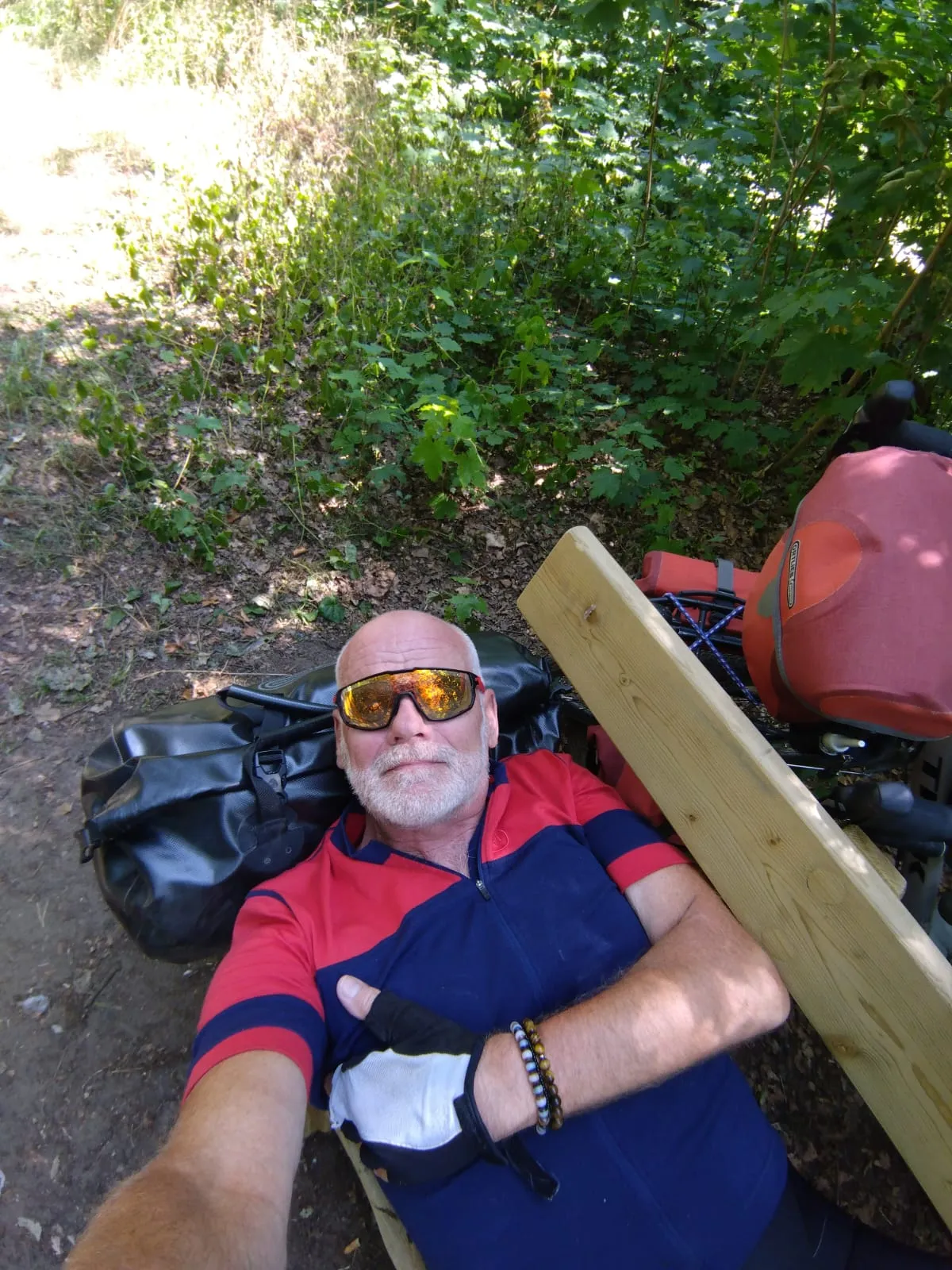 Jean-Pierre se repose sur un banc à l’ombre, avec ses sacoches à côté de lui