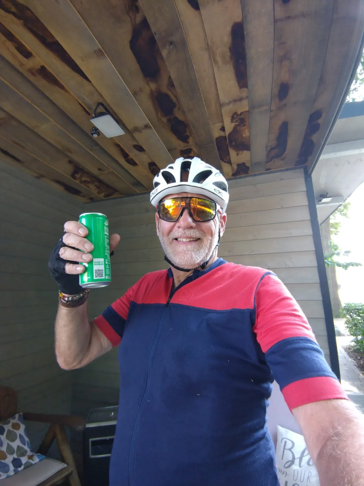 Jean-Pierre pose en tenue de cycliste sous un abri, une boisson à la main