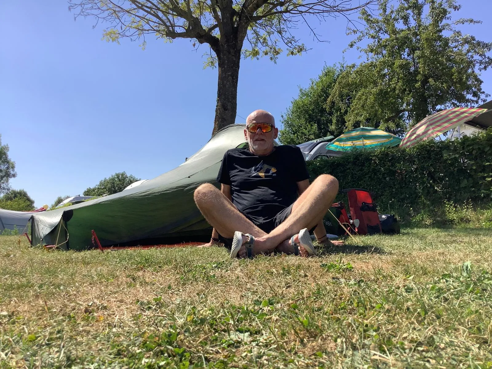 Jean-Pierre assis dans l’herbe devant sa tente au camping