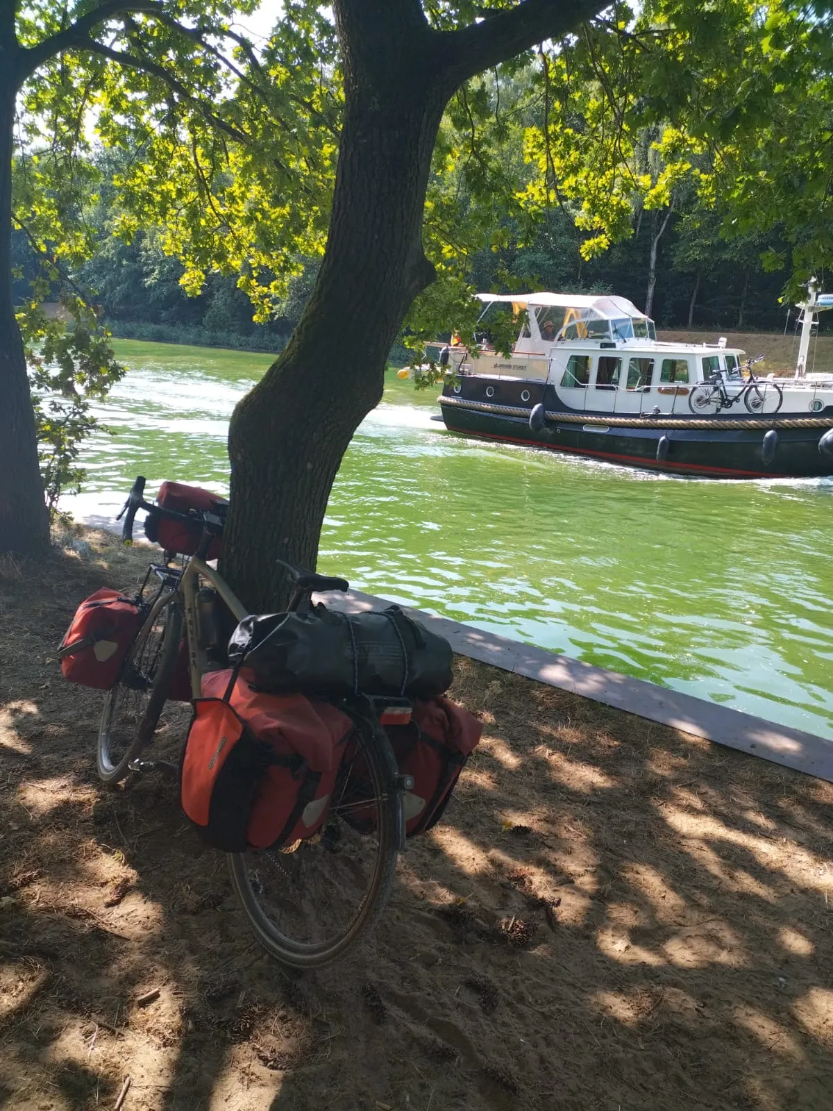 Le vélo chargé de Jean-Pierre au bord du canal, avec un bateau en arrière-plan